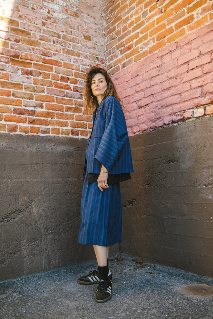 Blue striped button-up shirt with a relaxed, oversized fit, wide sleeves, a pointed collar, and a slightly structured silhouette, blending a casual and contemporary aesthetic.