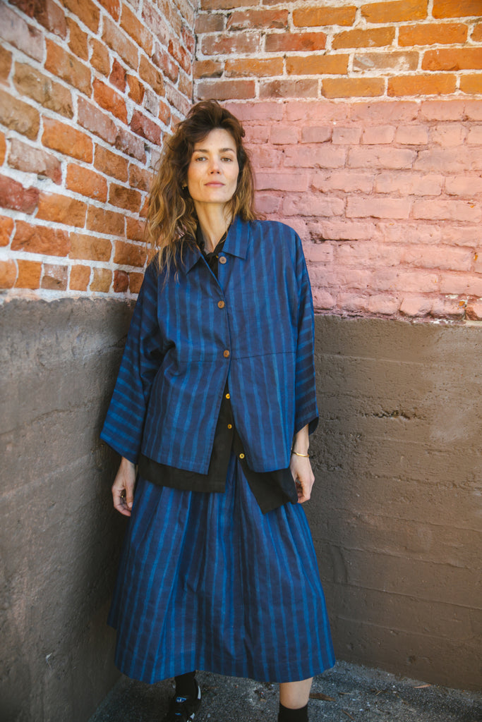 Blue striped button-up shirt with a relaxed, oversized fit, wide sleeves, a pointed collar, and a slightly structured silhouette, blending a casual and contemporary aesthetic.