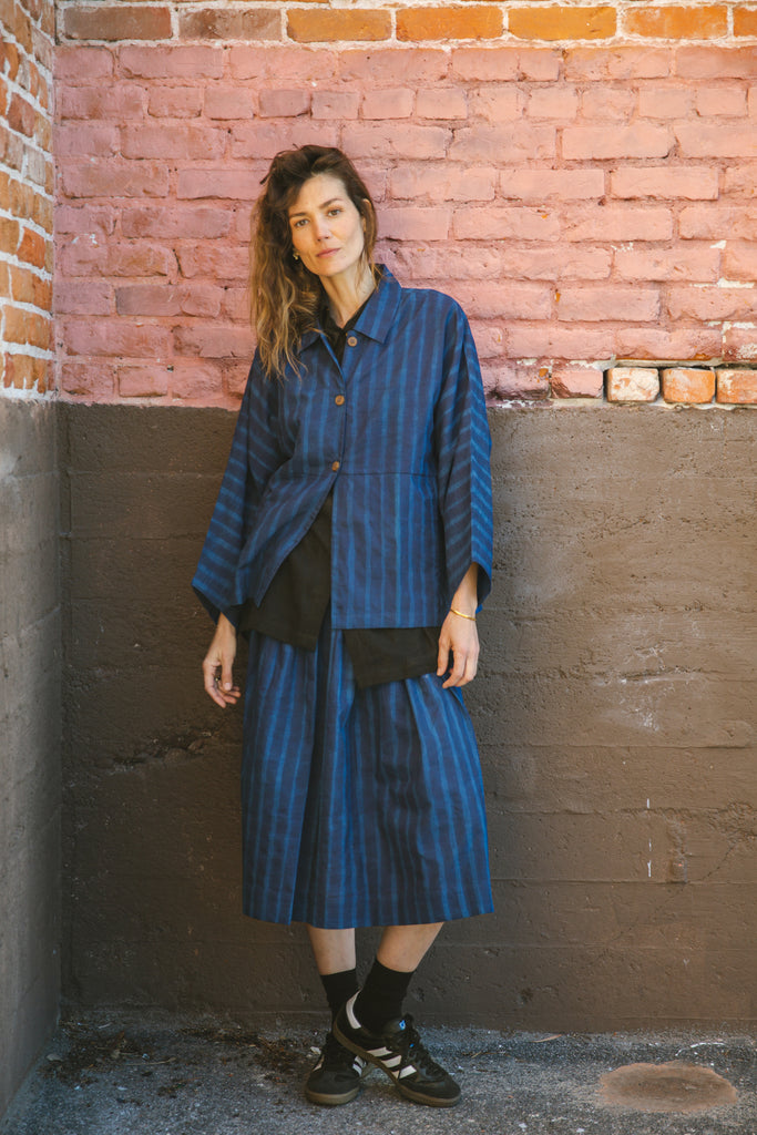 Blue striped button-up shirt with a relaxed, oversized fit, wide sleeves, a pointed collar, and a slightly structured silhouette, blending a casual and contemporary aesthetic.