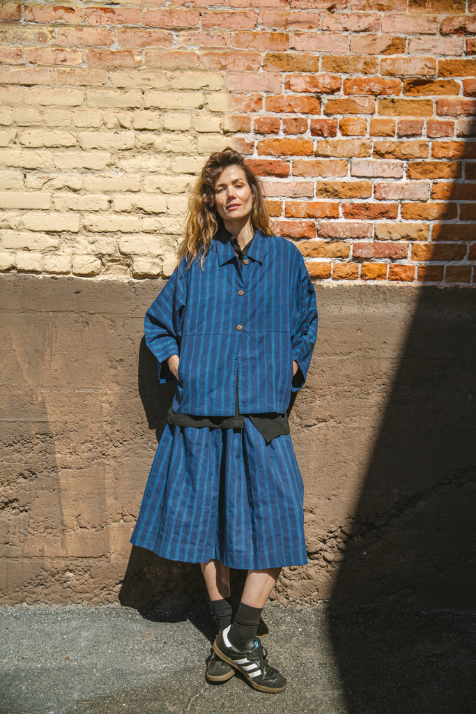 Blue striped button-up shirt with a relaxed, oversized fit, wide sleeves, a pointed collar, and a slightly structured silhouette, blending a casual and contemporary aesthetic.