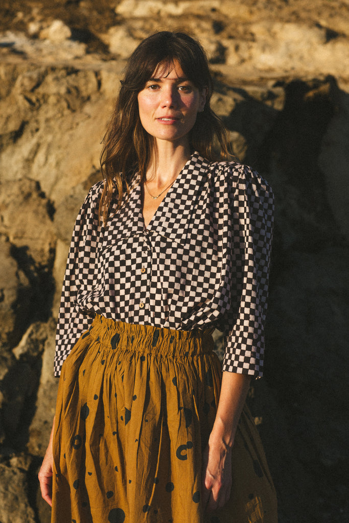 A black and white checkered blouse with a Victorian collar paired with a yellow skirt, showcasing vintage elegance.