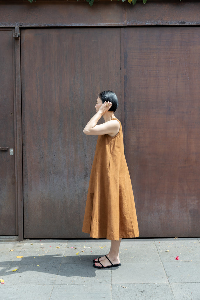 Sleeveless caramel-brown A-line midi dress with a high, round neckline. Features a voluminous flared silhouette, creating a breezy and effortless look. Made from textured, lightweight fabric for a natural, flowy drape.