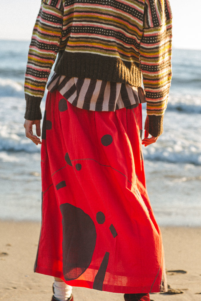 A bold red skirt with brown accents, showcasing unique appliqué craftsmanship and a versatile mid-calf length.