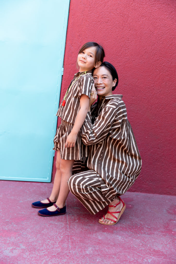 A short-sleeved, brown-and-white striped button-up shirt with a structured collar. The shirt has a relaxed fit and a slightly cropped length, giving it a casual and comfortable look. Made from lightweight fabric, it pairs seamlessly with matching striped shorts for a coordinated outfit.