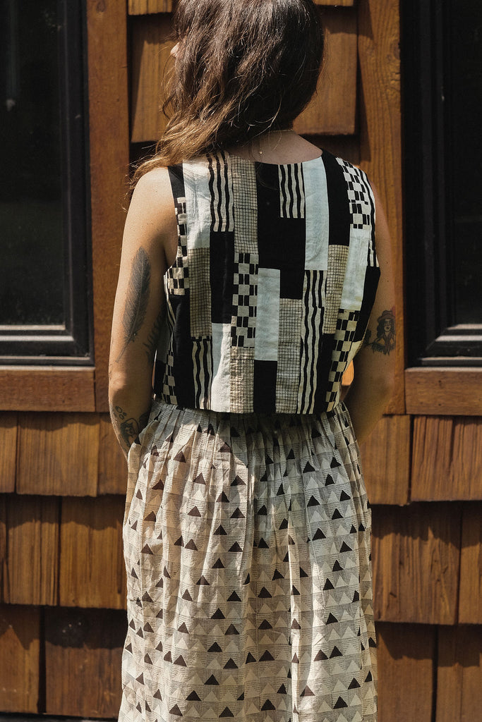 A mid-length, handwoven skirt made from soft, breathable organic cotton. The fabric features a delicate, all-over triangular block print in muted tones of black and grey on an off-white base. Lightly gathered at the waist, the skirt flows into a relaxed, voluminous silhouette that offers both comfort and movement. Naturally dyed and finished with a subtle texture, the skirt has an earthy, artisanal feel ideal for everyday wear.