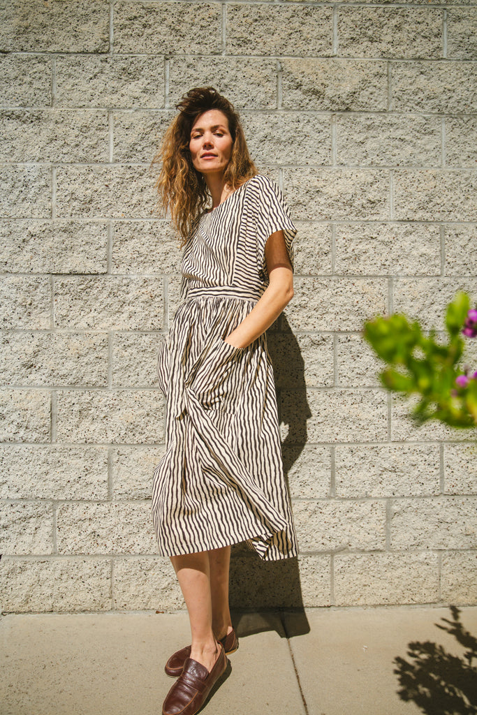 Black and white striped midi dress with short sleeves and an open-back design. Features a cinched waist with a tie detail for a flattering silhouette. Made from lightweight, breathable fabric, perfect for warm weather. A stylish choice for casual and semi-formal occasions.