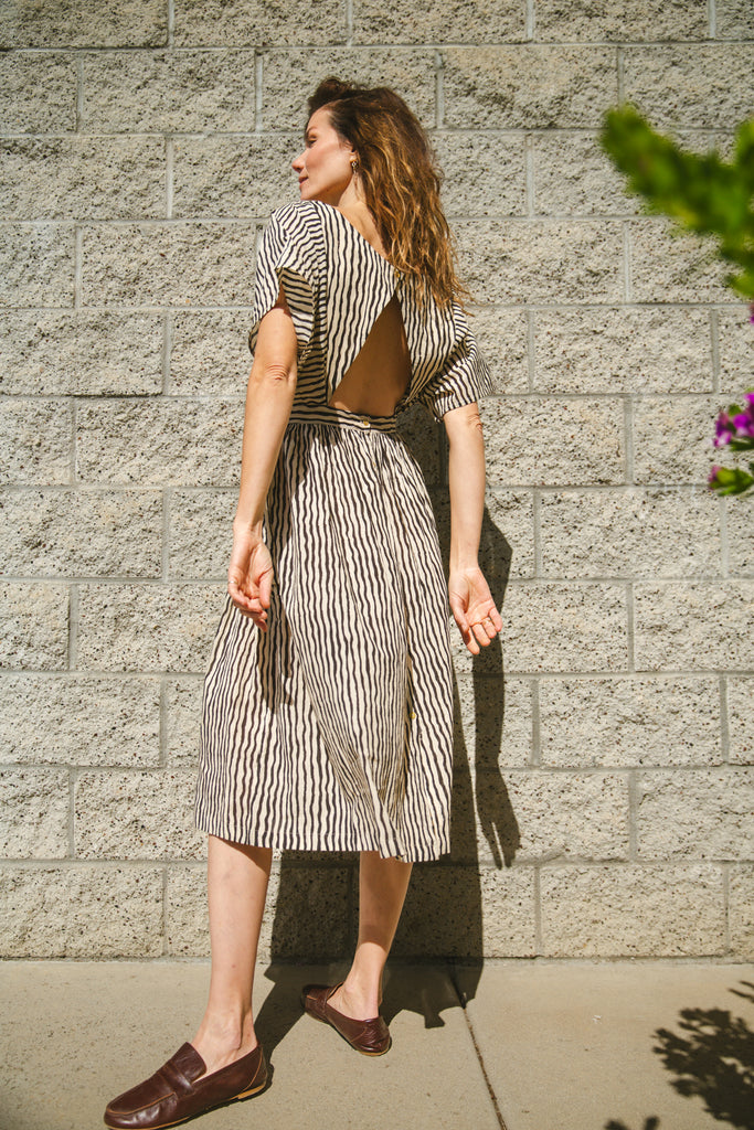 Black and white striped midi dress with short sleeves and an open-back design. Features a cinched waist with a tie detail for a flattering silhouette. Made from lightweight, breathable fabric, perfect for warm weather. A stylish choice for casual and semi-formal occasions.