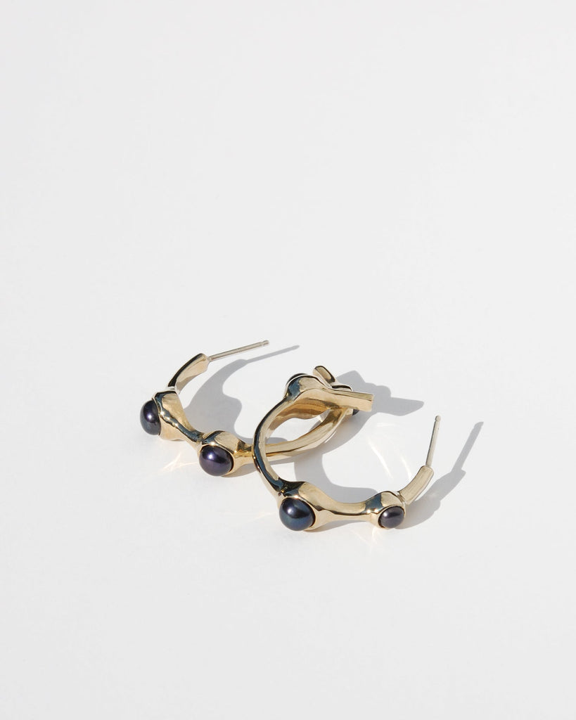 Introducing our Gold coloured Hoop Earrings adorned with three striking black pearls. Crafted in solid brass or sterling silver, these elegant earrings feature a slightly asymmetrical design, with a refined 1 1/4" diameter. Perfect for making a sophisticated statement, they blend timeless elegance with a touch of modern flair.