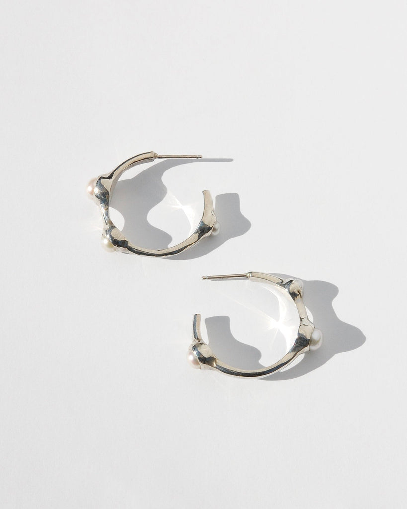 Introducing our elegant silver hoop earrings, featuring a sophisticated asymmetrical design with white pearls in varying sizes—3 mm, 4 mm, and 5 mm. Handcrafted with precision, these earrings are adorned with sterling silver posts and backs. Each pair is made to order and ships in 2-4 weeks, ensuring a unique addition to your collection.