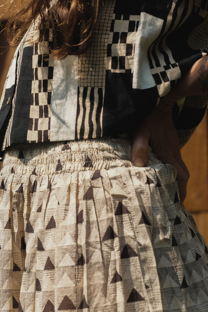 Sleeveless black and ivory patchwork top made from 100% organic cotton, featuring hand block-printed geometric patterns. Ethically crafted with a mix of stripes, checks, and textured prints using azo-free dyes. Lightweight, breathable fabric with a structured yet comfortable fit—perfect for summer styling or layering. Each piece is unique, showcasing subtle variations in print and color due to its handcrafted nature.