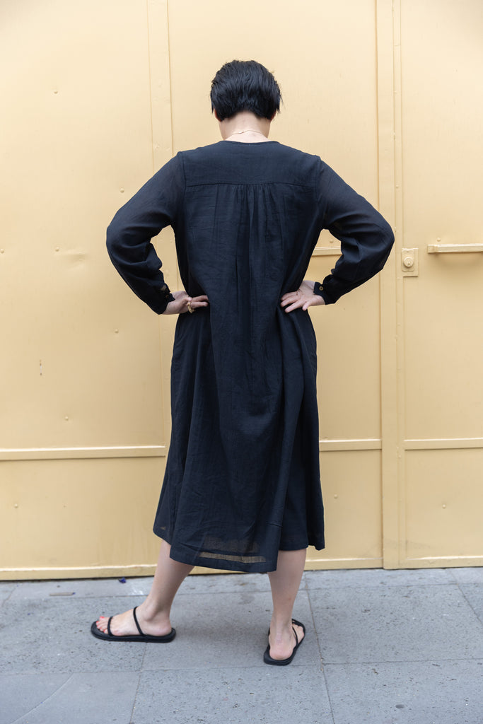 Black midi dress with long sleeves, a deep V-neckline with delicate gathers, and adjustable tie details. Designed with a relaxed waist and flowy fabric for effortless movement.