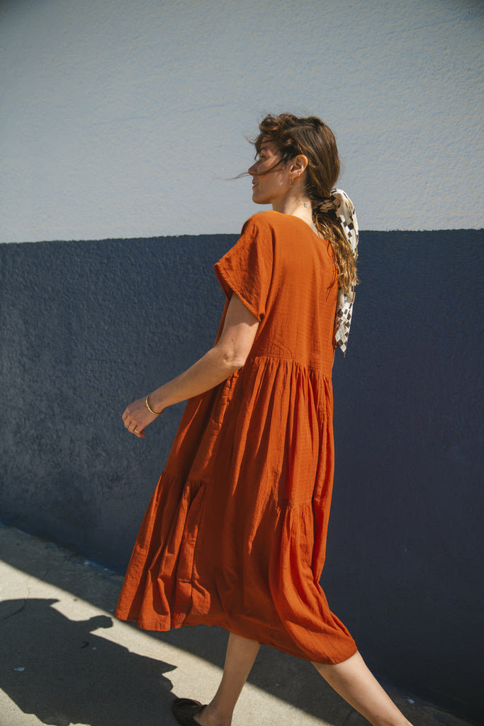 Rust orange tiered midi dress with a relaxed fit, short sleeves, a round neckline with a buttoned placket, and soft, lightweight fabric for an effortless, breezy style.