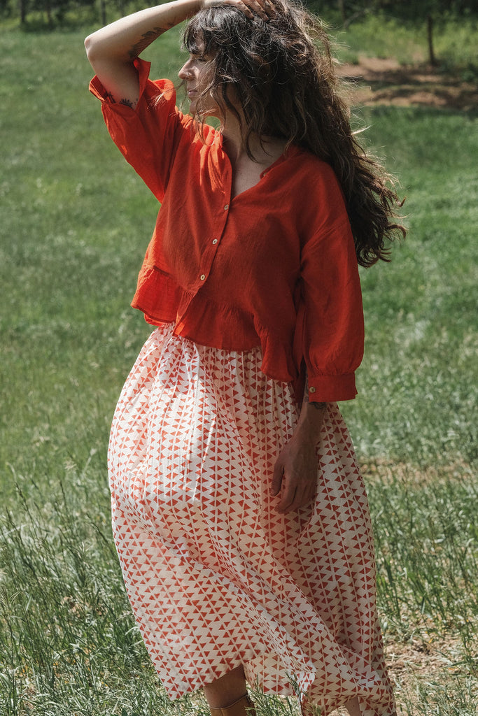 A lightweight, mid-length skirt by World of Crow featuring a soft, flowing texture that moves gracefully with the breeze. The skirt is crafted in a gentle off-white base adorned with hand-printed rust-red geometric motifs, creating a subtle yet striking pattern. Designed with a relaxed silhouette and gathered waist, it exudes an effortless, breezy charm perfect for warm, sunlit days. The fabric is  airy and breathable, offering comfort and elegance in equal measure.