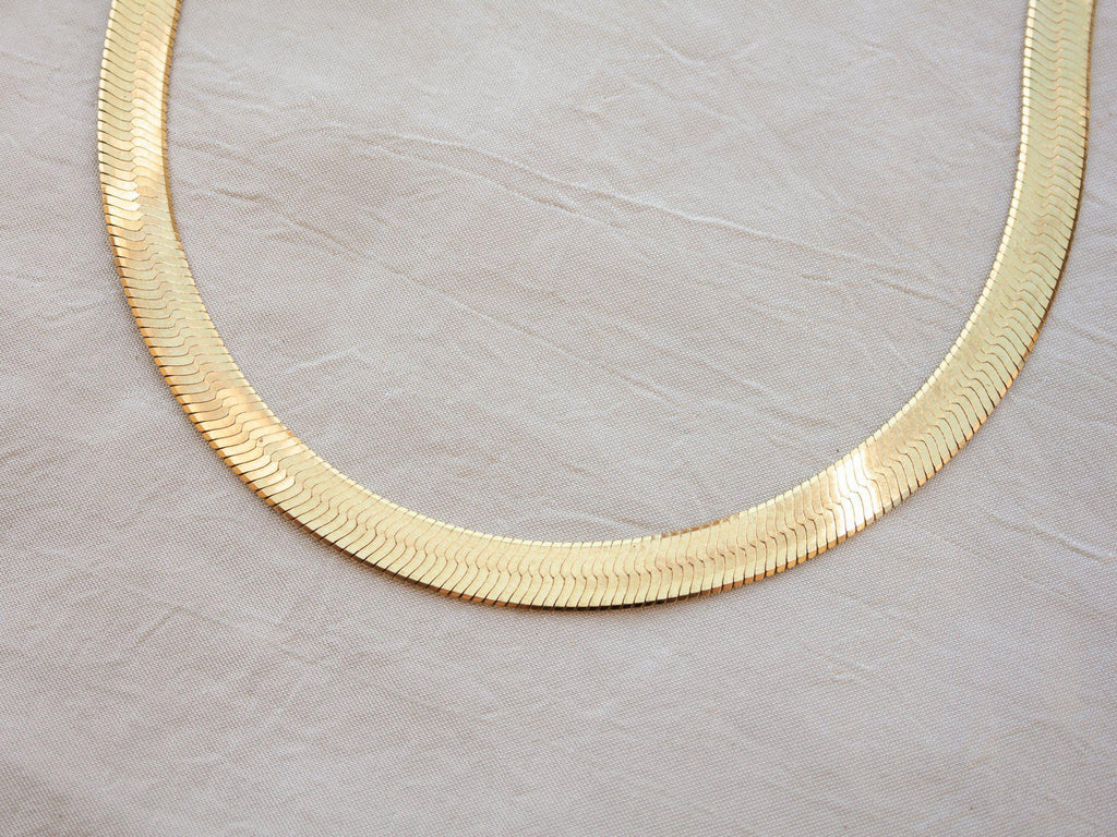 Introducing our gold herringbone necklace, a vintage-inspired statement piece made in Italy. This necklace features a striking 18" length and 7mm thickness, elegantly plated in 14k yellow gold. Its classic design and luxurious finish make it a timeless addition to any jewelry collection.